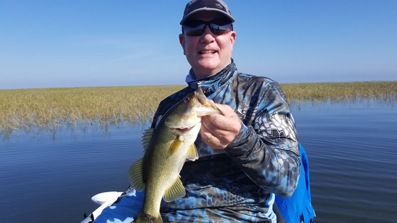 Angler holding a Lake Okeechobee largemouth bass near grass