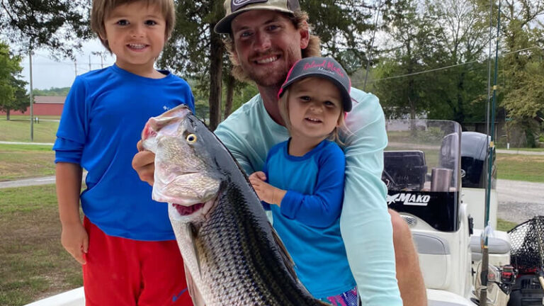Angler and two children holding a large striped bass beside a fishing boat