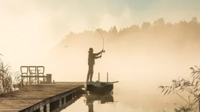 Fisherman casting a line with underspin swimbaits for bass on a misty lake at sunrise.