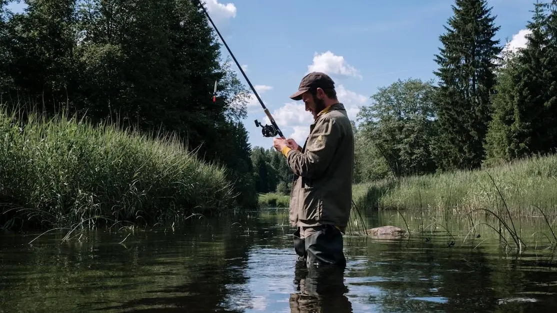 Man creek fishing for largemouth in a serene forest river.