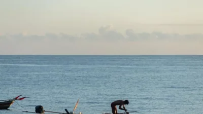 Fisherman at sunrise, preparing boat on calm ocean—ideal travel insurance for fishing trips.