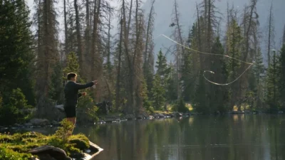 Angler flipping and pitching for bass in a serene alpine lake at sunrise.