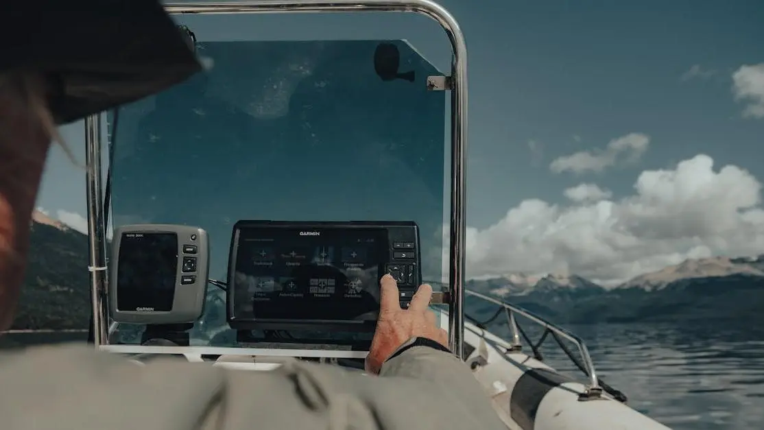 Angler using fish finder and GPS to read bass fishing electronics on a lake with mountain view